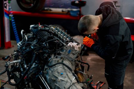 Photo for At a service station a young master repairs a motor part removed from a car for a complete overhaul - Royalty Free Image