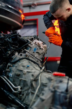 Foto de Primer plano En una estación de servicio un joven maestro repara una pieza de motor retirada de un coche para una revisión completa - Imagen libre de derechos