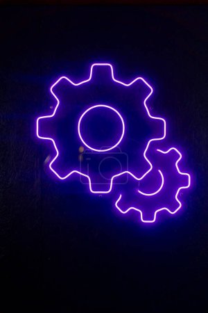 Photo for Close-up At a service station a neon sign in the shape of a gear for oil hangs on the wall purple light - Royalty Free Image