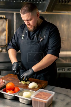 in einer professionellen Küche hackt ein Koch in schwarzer Uniform Zwiebeln auf einem Brett