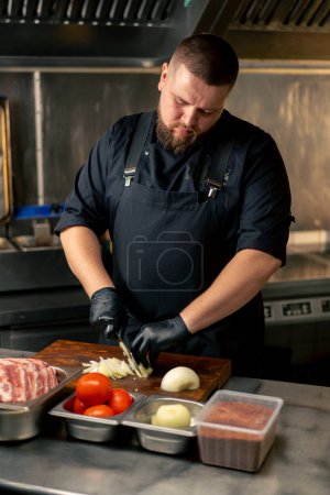 in einer professionellen Küche hackt ein Koch in schwarzer Uniform Zwiebeln auf einem Brett