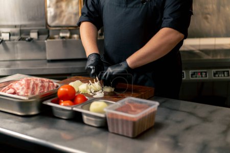 hautnah in einer professionellen Küche schneidet ein Koch in schwarzer Uniform Zwiebeln auf einem Brett