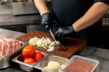 Foto de Primer plano en una cocina profesional un chef en un uniforme negro cebollas chuletas en una tabla - Imagen libre de derechos