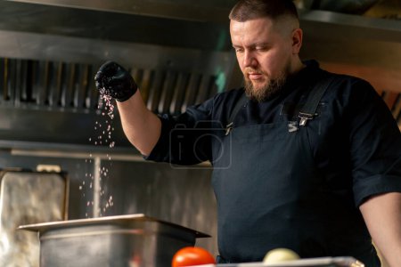 Foto de En cocina profesional en un chef en una chaqueta negra sales y pimientos costillas en un tazón de hierro - Imagen libre de derechos