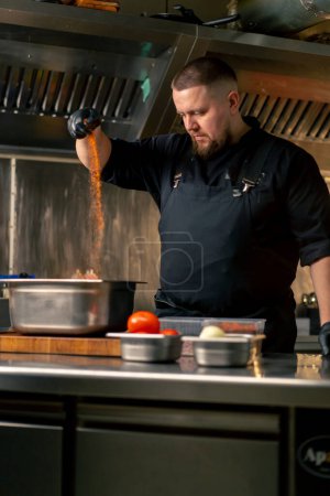 in der professionellen Küche in einem Koch in einer schwarzen Jacke Salz und Paprika Rippen in einer eisernen Schüssel