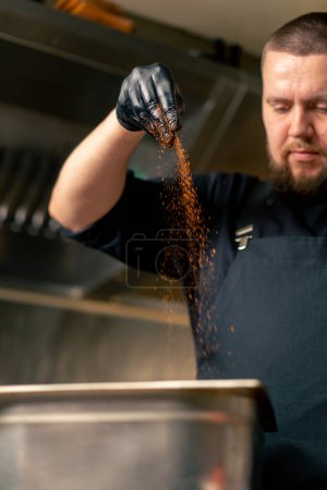 Téléchargez les photos : Gros plan dans la cuisine professionnelle dans un chef dans une veste noire sels et poivrons côtes dans un bol de fer - en image libre de droit