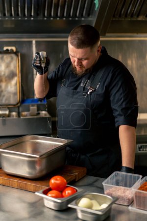 in der professionellen Küche gießt ein Koch in schwarzer Jacke Öl in eine eiserne Schüssel