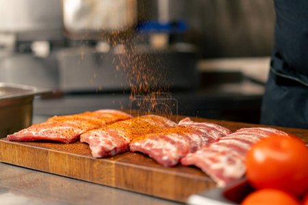Nahaufnahme in der professionellen Küche in einem Koch im schwarzen Sakko salzt und pfeffert Rippen