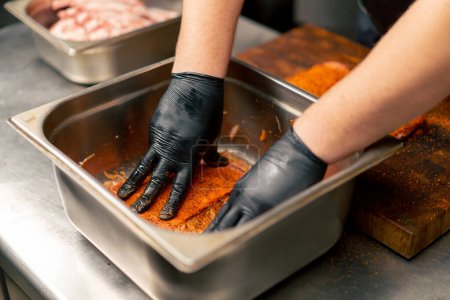 Nahaufnahme in einer professionellen Küche in Koch in schwarzen Handschuhen mariniert Rippen in einer eisernen Schüssel