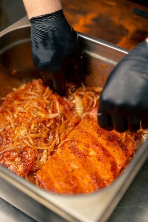 Nahaufnahme in einer professionellen Küche in Koch in schwarzen Handschuhen mariniert Rippen in einer eisernen Schüssel