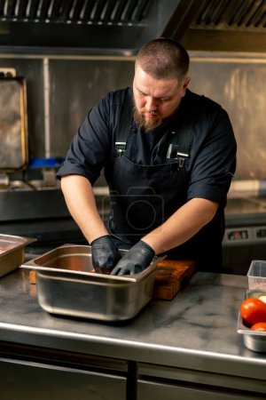 in einer professionellen Küche mariniert Koch in schwarzen Handschuhen Rippen in einer eisernen Schüssel