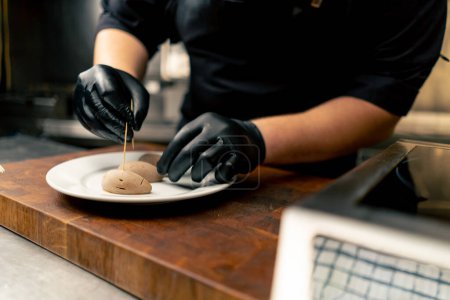 Téléchargez les photos : Gros plan dans une cuisine professionnelle chef en gants noirs insère cure-dents dans une délicatesse - en image libre de droit