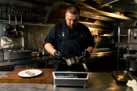 en un chef de cocina profesional en una chaqueta negra mezcla la salsa en una cacerola