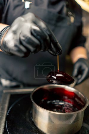 primer plano en un chef de cocina profesional en guantes negros empapa una delicadeza en una salsa de color burdeos de una sartén