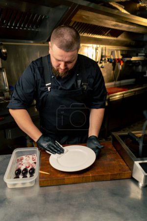 Photo for In a professional kitchen chef in a black tunic wipes the plate dry before laying out the delicacy - Royalty Free Image