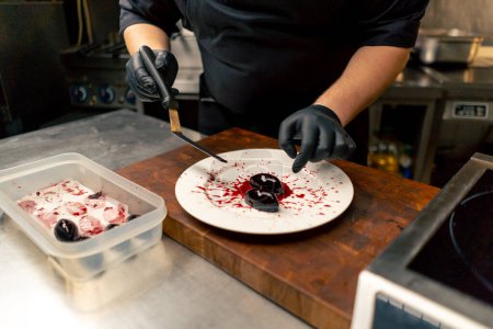 in professional kitchen with a chef in black gloves laying out dessert on a plate