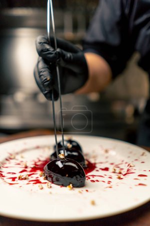 Foto de Primer plano en una cocina profesional el chef en guantes negros decora el postre con pinzas - Imagen libre de derechos