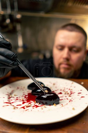 close-up in a professional kitchen the chef in black gloves decorates the dessert with tweezers