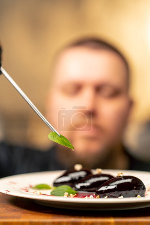Téléchargez les photos : Close-up dans une cuisine professionnelle le chef en gants noirs décore le dessert avec une pince à épiler - en image libre de droit