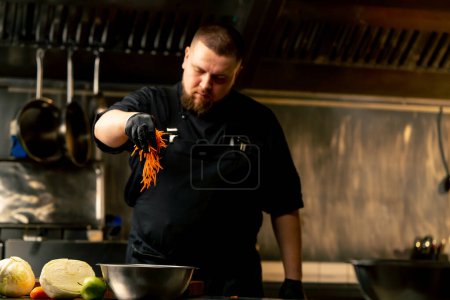 in einer professionellen Küche mit schwarzen Handschuhen schüttet Karottenstäbchen in eine eiserne Schüssel
