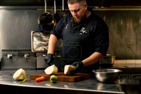 in einer professionellen Küche mit schwarzen Handschuhen schneidet Kohl auf Holzbrett