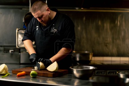 Téléchargez les photos : Dans une cuisine professionnelle portant des gants noirs coupe le chou sur une planche de bois - en image libre de droit