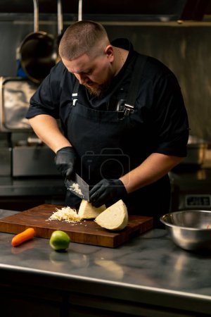 in a professional kitchen wearing black gloves cuts cabbage on wooden board