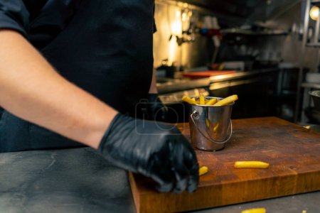 Téléchargez les photos : Gros plan dans la cuisine professionnelle le chef verse des frites dans un seau de fer - en image libre de droit