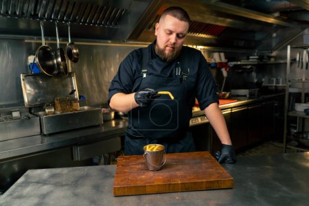 Foto de En una cocina profesional un chef en una chaqueta negra sabe a papas fritas recién preparadas - Imagen libre de derechos