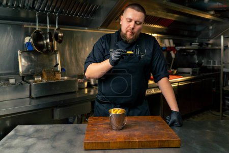 Téléchargez les photos : Dans une cuisine professionnelle, un chef en veste noire goûte les frites fraîchement préparées - en image libre de droit