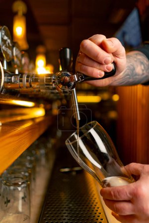 Téléchargez les photos : Gros plan dans la brasserie au comptoir du bar les mains des barmans versent de la bière légère dans un verre - en image libre de droit