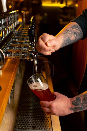 Photo for Close-up in beer hall at the bar counter the bartenders hands pour light beer into a glass - Royalty Free Image