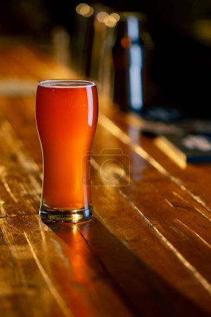 Foto de Primer plano en el bar hay un vaso de cerveza en un mostrador de bar de madera en los rayos del sol - Imagen libre de derechos