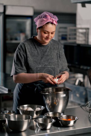 Foto de En una cocina profesional sobre una mesa de hierro panadero rompe un huevo en un tazón de hierro grande - Imagen libre de derechos