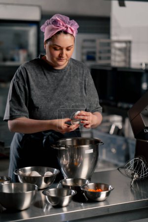 Foto de En una cocina profesional sobre una mesa de hierro panadero rompe un huevo en un tazón de hierro grande - Imagen libre de derechos