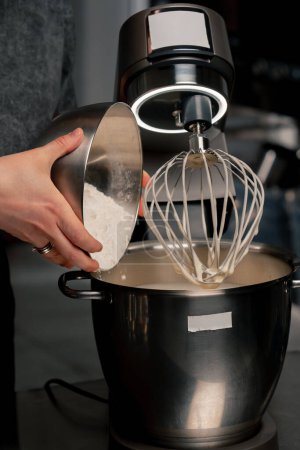 Nahaufnahme der Hände in einer professionellen Küche über einem eisernen Tisch: Ein Bäcker gießt Mehl in einen Mixer