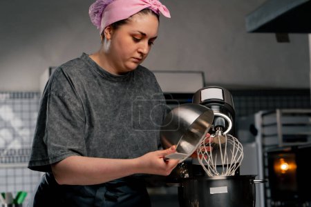 In einer professionellen Küche gießt ein Bäcker über einem Eisentisch Mehl in einen Mixer