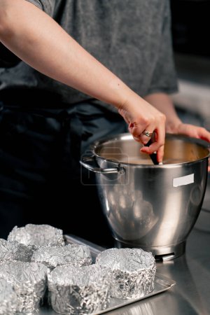 Foto de Primer plano de las manos en una cocina profesional mezclando masa preparándose para verter en moldes - Imagen libre de derechos