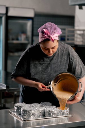 panadero femenino en una cocina profesional vierte masa en capas de moldes de pastel