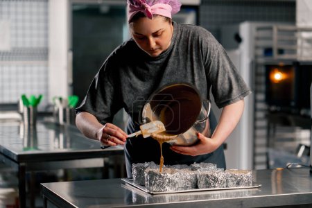 Foto de Panadero femenino en una cocina profesional vierte masa en capas de moldes de pastel - Imagen libre de derechos