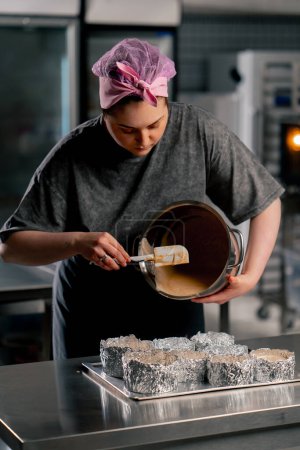 panadero femenino en una cocina profesional vierte masa en capas de moldes de pastel