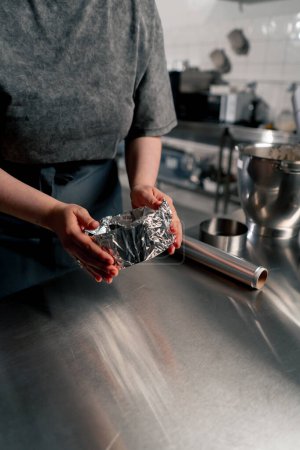 Foto de Cerrar las manos panadero en una cocina profesional envuelve las sartenes con papel de aluminio antes de verter la masa sobre el pastel - Imagen libre de derechos