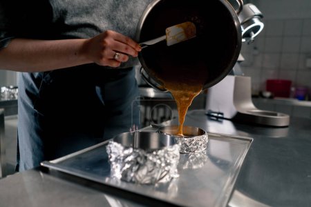 Foto de Cerrar las manos panadero femenino en una cocina profesional vierte masa en capas de moldes de pastel - Imagen libre de derechos
