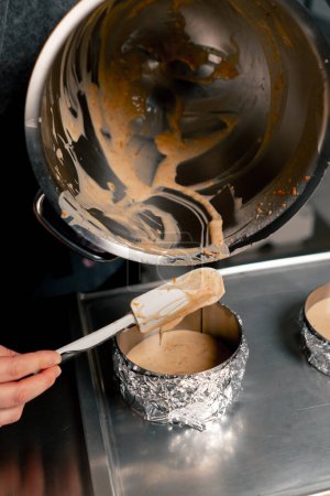 cerrar las manos panadero femenino en una cocina profesional vierte masa en capas de moldes de pastel