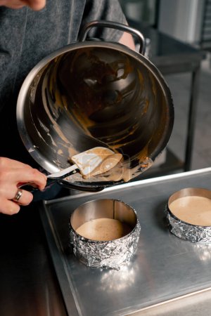 Téléchargez les photos : Fermer les mains boulanger femelle dans une cuisine professionnelle verse la pâte en couches de moules à gâteau - en image libre de droit