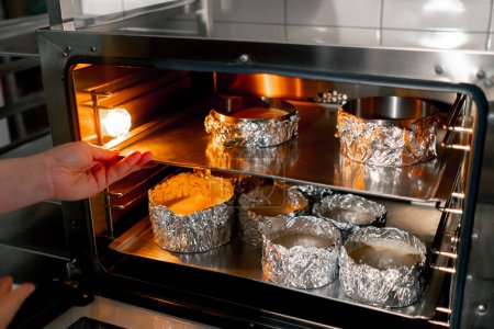 Téléchargez les photos : Dans une cuisine professionnelle, un boulanger insère une plaque de cuisson avec moules à gâteau dans le four - en image libre de droit