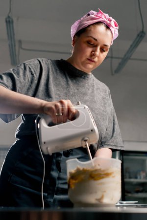 Foto de Panadero femenino en una pasta de látigos de cocina profesional para crema en un pastel con una batidora - Imagen libre de derechos