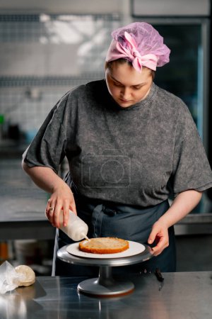 Foto de Panadero femenino en una cocina profesional empapando una torta de esponja antes de aplicar crema - Imagen libre de derechos