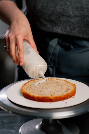 Téléchargez les photos : Fermer boulanger femelle dans une cuisine professionnelle tremper un gâteau éponge avant d'appliquer de la crème - en image libre de droit