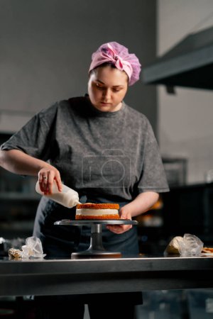 Foto de Panadero femenino en una cocina profesional empapando una torta de esponja antes de aplicar crema - Imagen libre de derechos